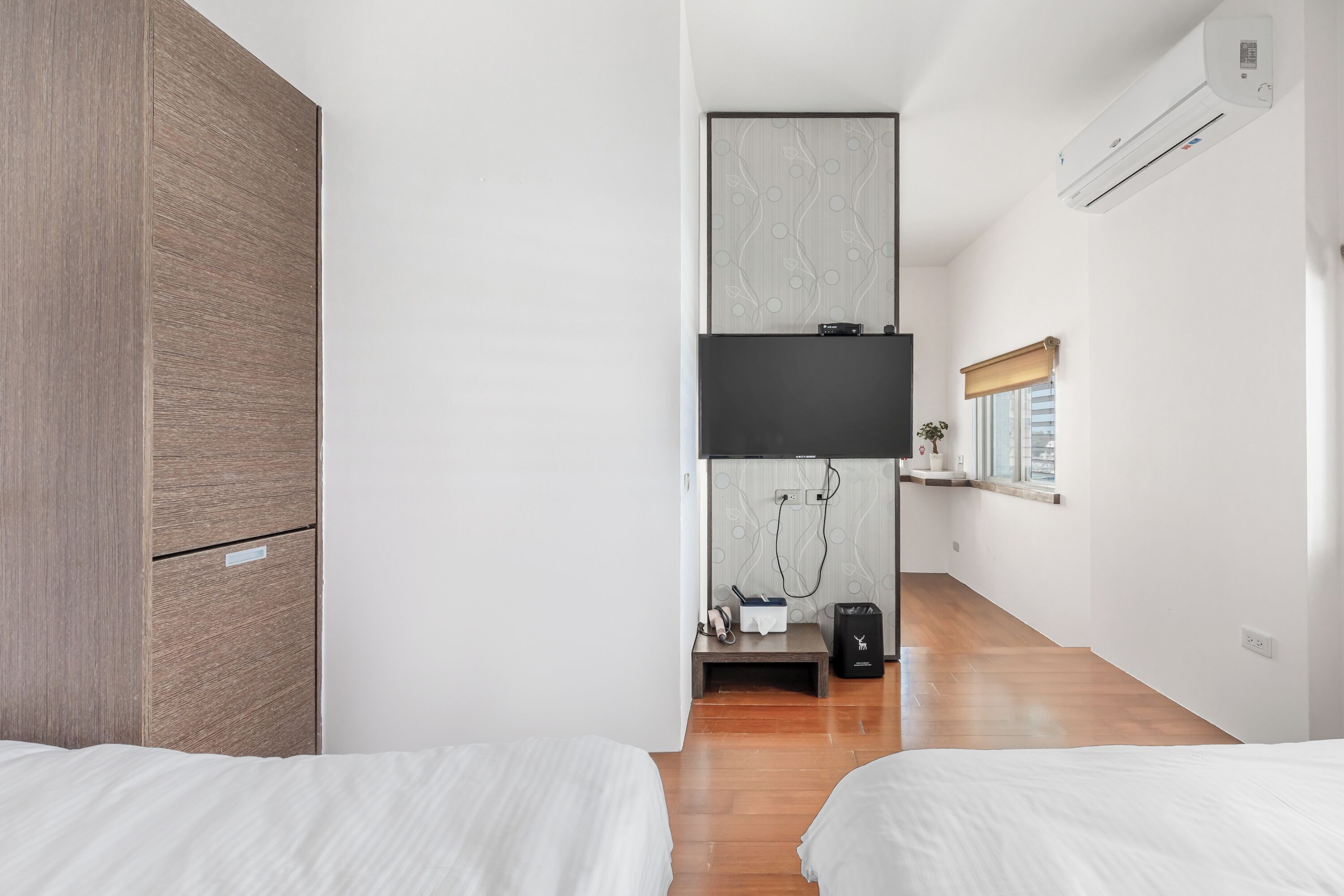 A modern hotel room with two beds, a wooden wardrobe, a flat-screen TV, a shower area, and a window with a view.