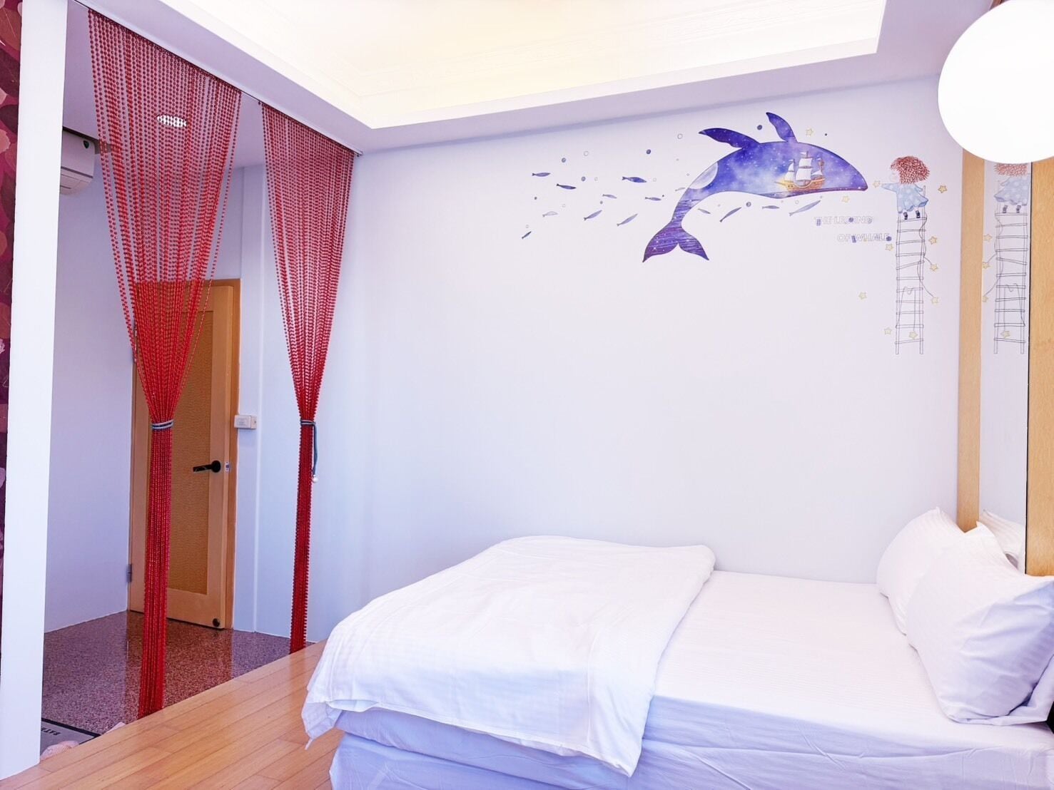 A bedroom with a bed, a wall mural of a whale, and a red curtain.
