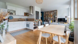 Uma cozinha moderna com armários brancos, uma mesa de jantar de madeira e uma estante repleta de livros.