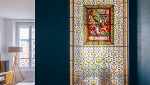 Quarto com uma grande janela de vitrais, piso de madeira, uma cadeira branca e uma planta.