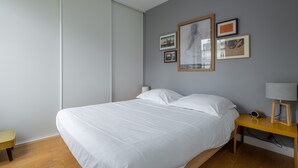 Quarto moderno com uma cama grande, mesa de cabeceira com abajur e obras de arte emolduradas na parede.