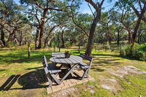 Una mesa de picnic al aire libre con bancos, rodeada de árboles y césped.