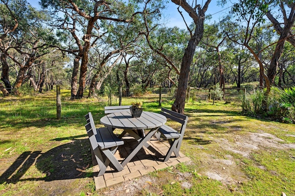 An outdoor picnic table with benches, surrounded by trees and grass.
