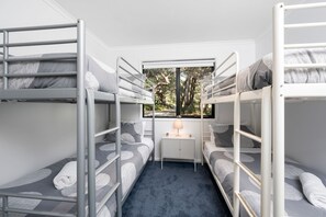 A bunk bed room with a window view of trees, a small bedside table with a lamp, and a blue carpet.