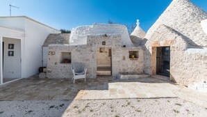 A stone building with a door and a small window, a chair, and a gravel courtyard. - Trullo La Dolina by Wonderful Italy (Ostuni)