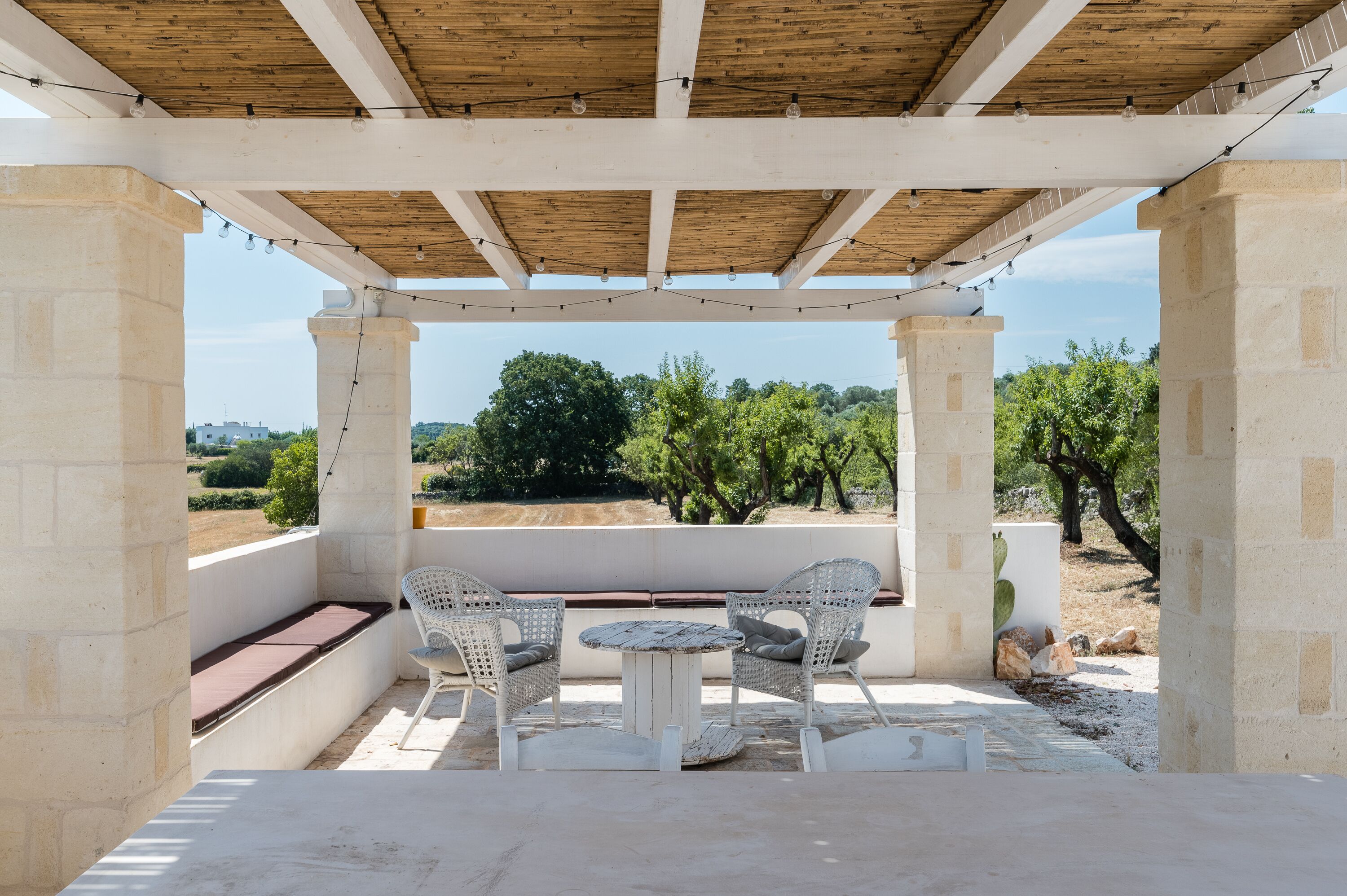 A covered outdoor seating area with a table and chairs, overlooking a landscape with trees and a distant view.
