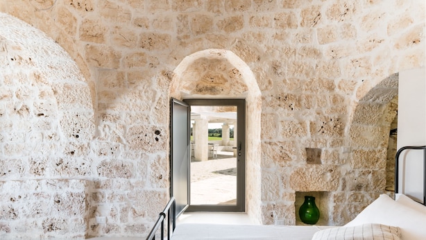 A room with stone walls, a bed with a pillow, a green vase, and a view through an open doorway. - Trullo La Dolina by Wonderful Italy (Ostuni)