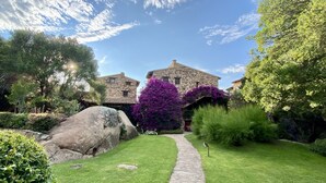 A stone building with a stone pathway leading to it, surrounded by lush greenery and large rocks. - AQUA GREEN HOUSE (Porto Rotondo)