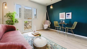 Un salon moderne avec une grande fenêtre, un fauteuil suspendu, une petite table ronde et un canapé.