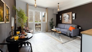Un salon moderne avec un canapé gris, une table à manger où est servi le petit-déjeuner, et une grande fenêtre.