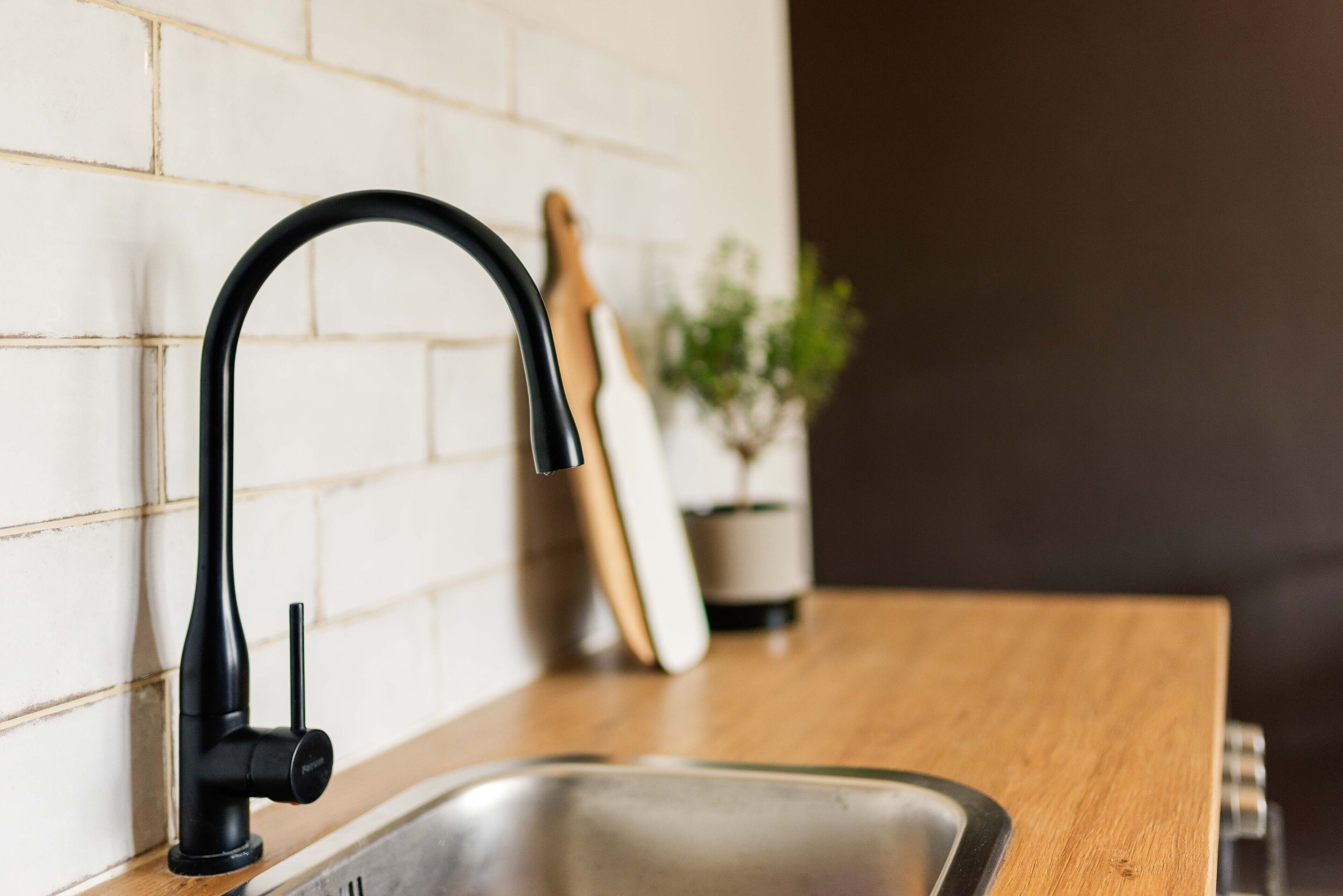 Una cocina moderna con un grifo negro, salpicadero de azulejos blancos y encimera de madera.
