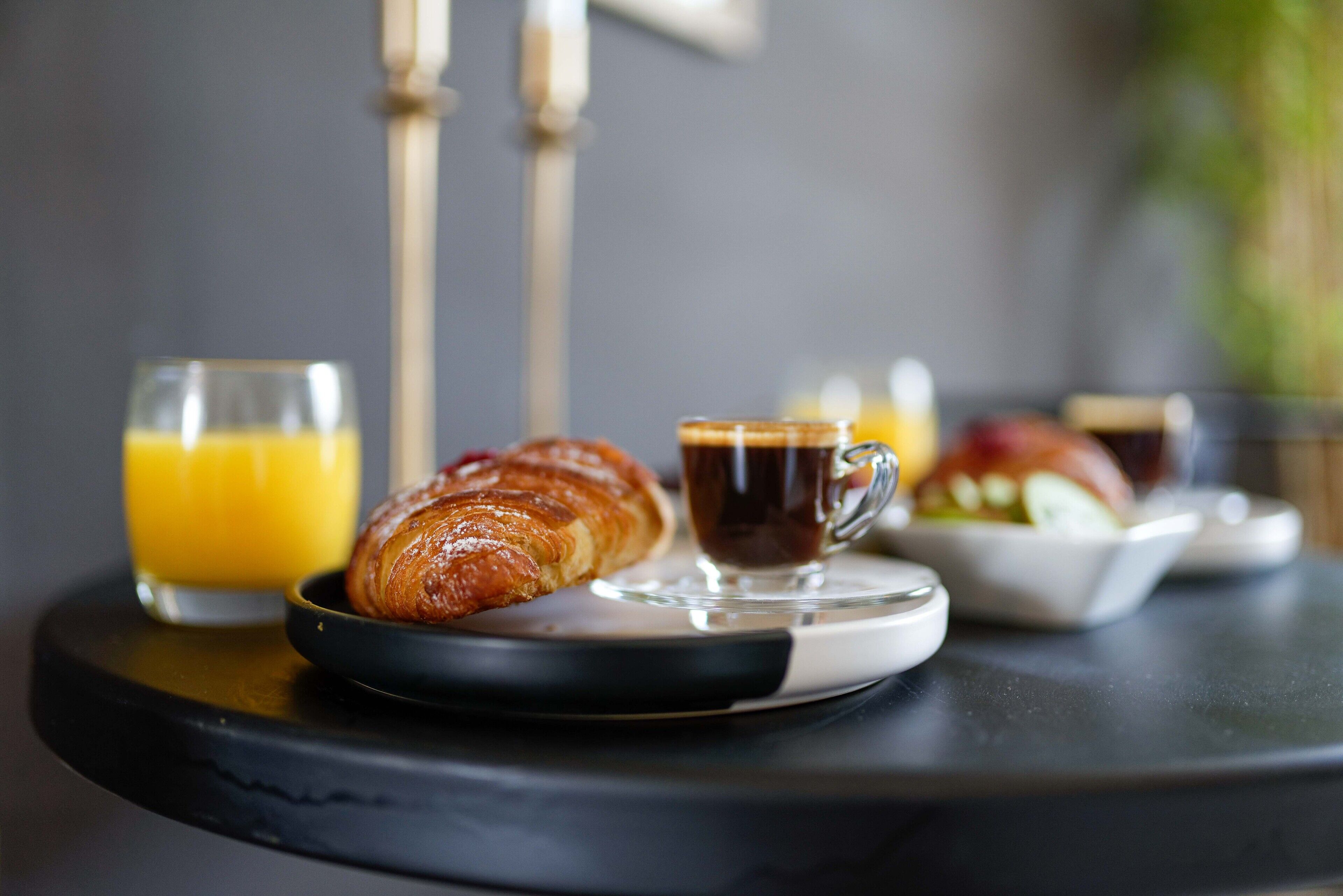 Uma mesa com um croissant, café e sumo de laranja para o pequeno-almoço.
