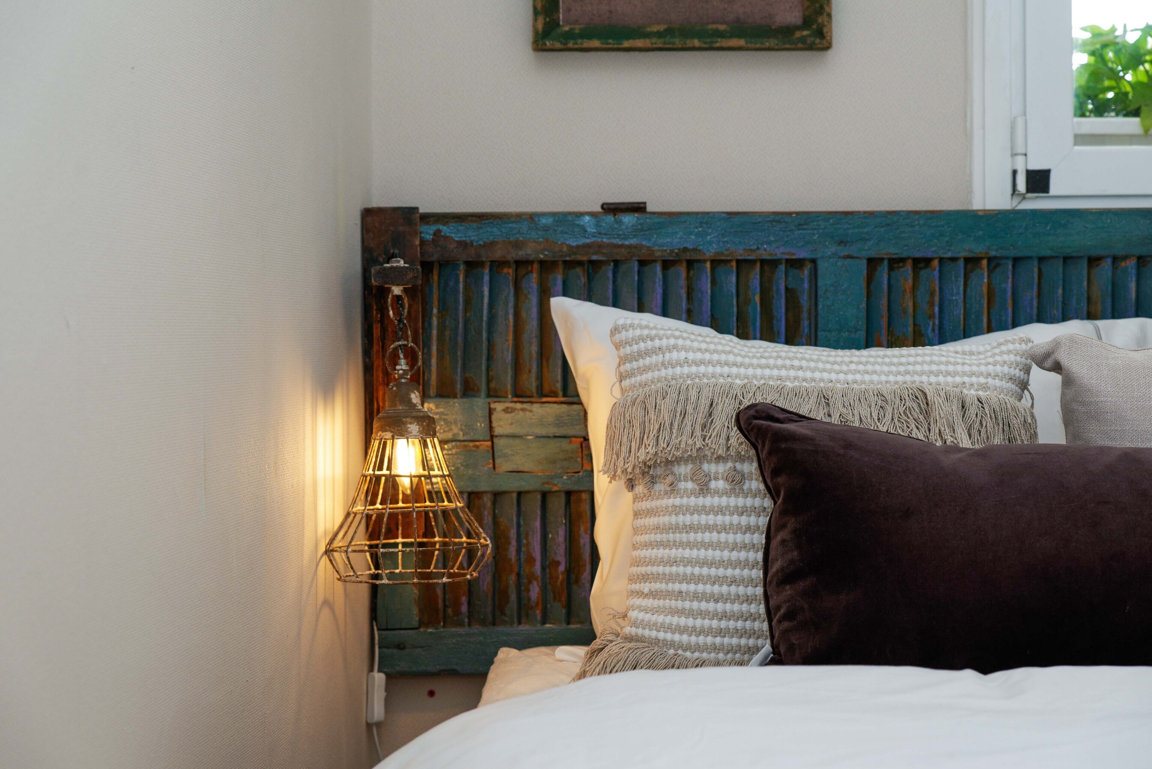 A bed with a wooden headboard, a wall-mounted light fixture, and a framed picture.