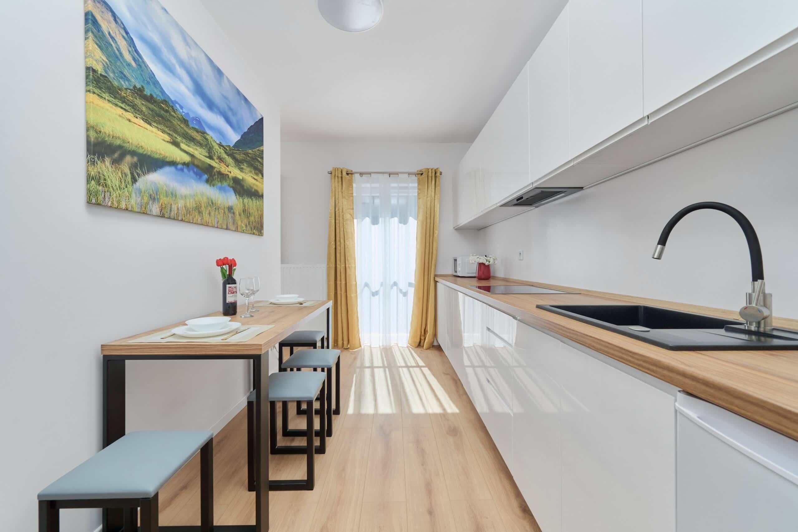 A modern kitchen with a wooden countertop, a black sink, and a view of a landscape painting.