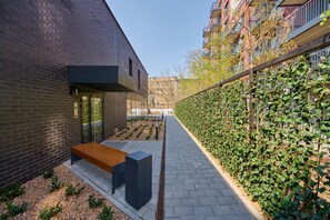 A modern building with a brick exterior, a bench, and a pathway lined with greenery.