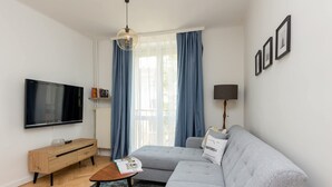 A modern living room with a grey sofa, a wooden side table, a flat-screen TV, and a floor lamp. - Comfortable Apartment in Downtown | A place to work (Warszawa)
