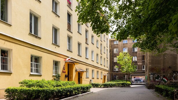 A courtyard with a yellow building, a tree, and a graffiti-covered wall. - Comfortable Apartment in Downtown | A place to work (Warszawa)