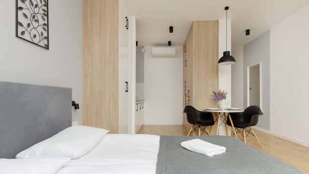 Habitación de hotel con cama, escritorio y dos sillas, una mesita con un florero y un equipo de aire acondicionado.