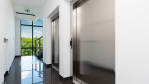 Un ascensor moderno con detalles metálicos, puerta de cristal y señalización visible de salida de emergencia.