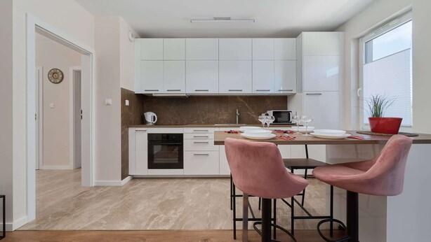 A modern kitchen with white cabinets, a marble countertop, and two pink bar stools. - Spacious Apartment | Balcony, Parking, Desk (Wroclaw)