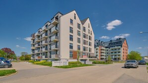 A multi-story residential building with balconies, a paved driveway, and a sign indicating the address. - Spacious Apartment | Balcony, Parking, Desk (Wroclaw)