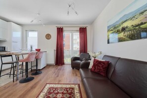 Ett modernt vardagsrum med en brun lädersoffa, en matplats med bord och stolar, ett kök med vita skåp och ett stort fönster med röda gardiner.