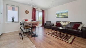 A living room with a sofa, a dining table with chairs, a red curtain, and a painting on the wall. - Spacious Apartment | Balcony, Parking, Desk (Wroclaw)
