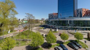 Un edificio moderno con fachada de vidrio, rodeado de un área de estacionamiento y vegetación.