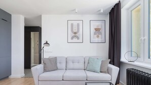 Un salón moderno con un sofá gris, dos obras de arte abstractas enmarcadas, una mesa de centro de vidrio y un radiador.