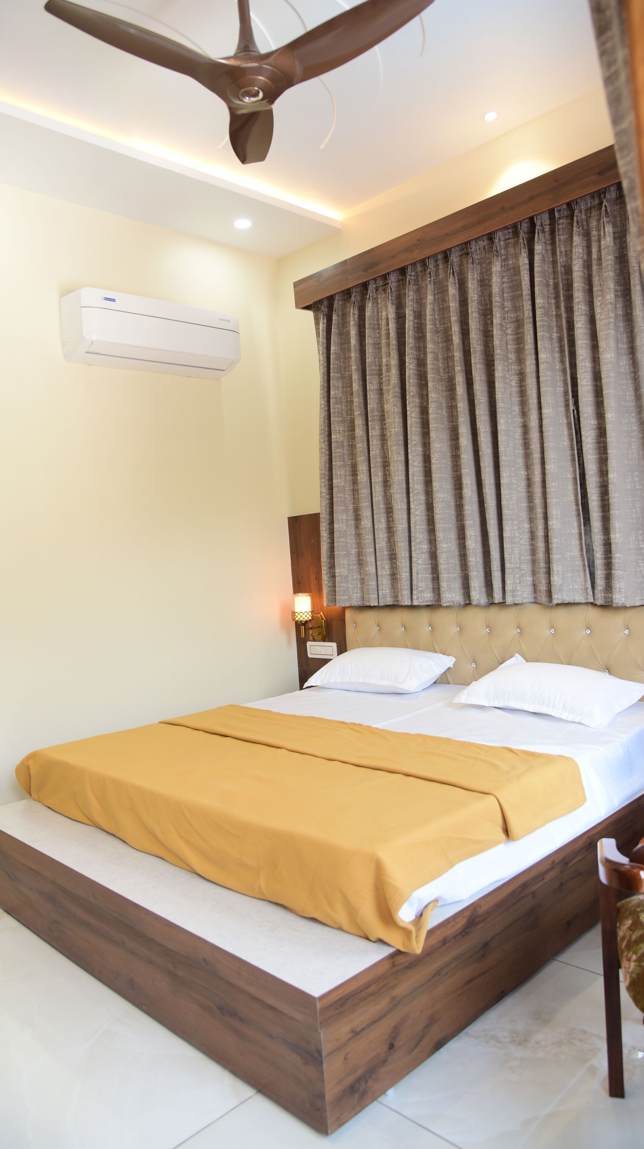 A bedroom with a bed, a ceiling fan, an air conditioning unit, and a nightstand with a lamp.