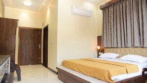 A hotel room with a bed, a desk, a chair, a wardrobe, and an air conditioning unit. - Naini Hill Inn (Haldwani)