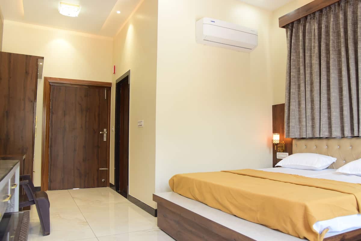 A hotel room with a bed, a desk, a chair, a wardrobe, and an air conditioning unit.