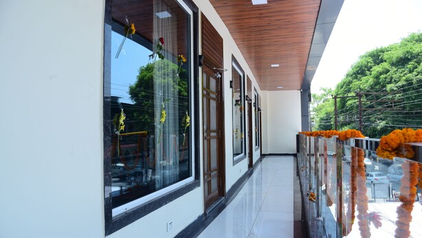 A corridor with large windows, a wooden ceiling, and a railing decorated with orange flowers. - Naini Hill Inn (Haldwani)