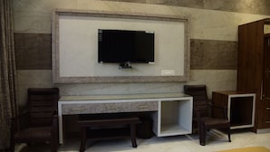 A modern office space with a large flat-screen TV mounted on a marble wall, a glass desk with two drawers, and two brown leather chairs. - Naini Hill Inn (Haldwani)