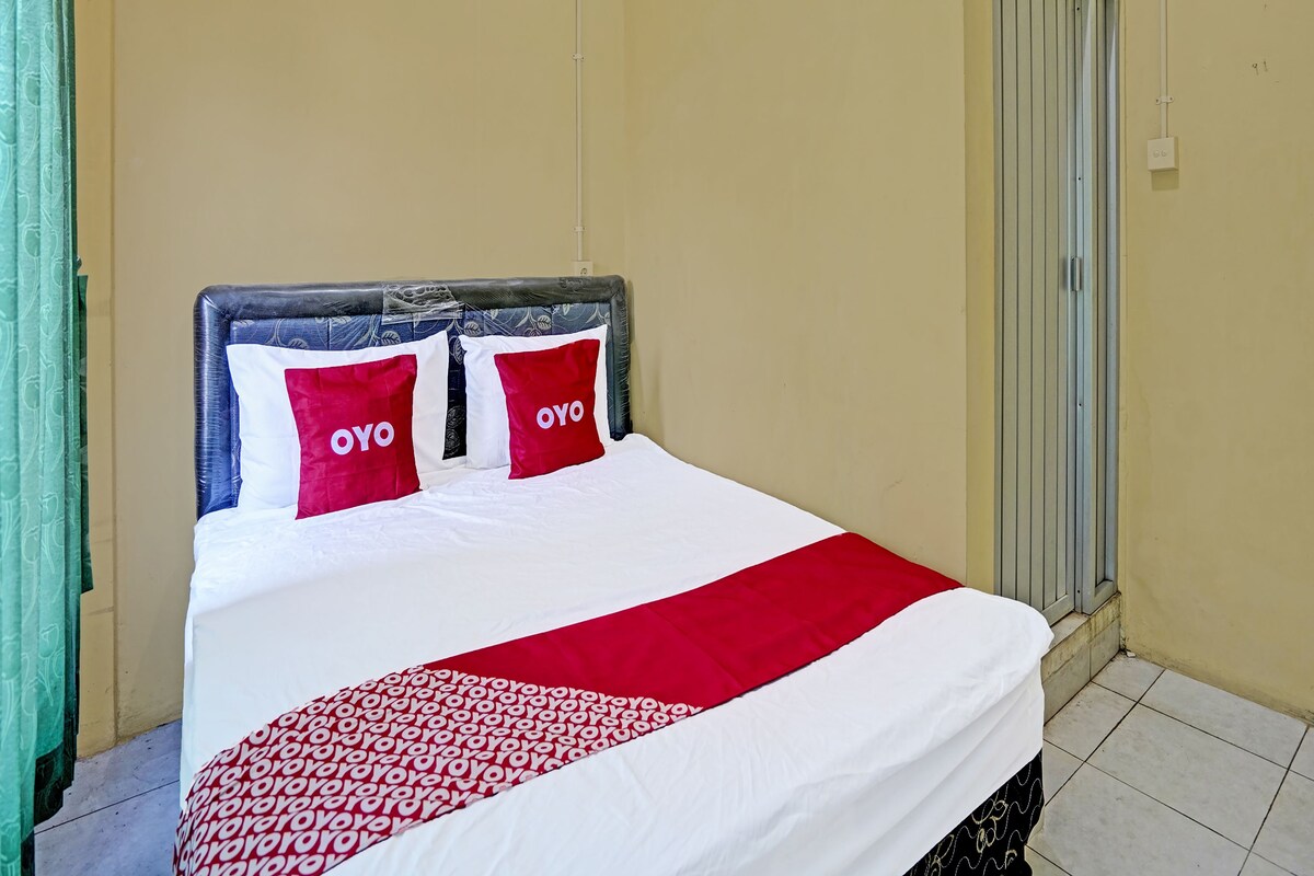 Un letto con biancheria da letto bianca e rossa, due cuscini con il marchio "OYO" e una corrimato rosso e bianco.