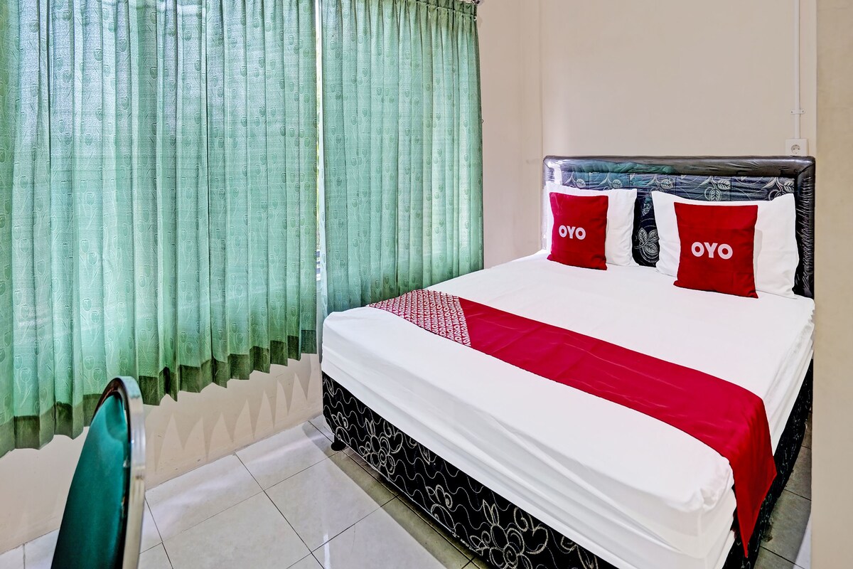 Camera d'albergo con un letto, tende verdi e due cuscini con il marchio OYO.