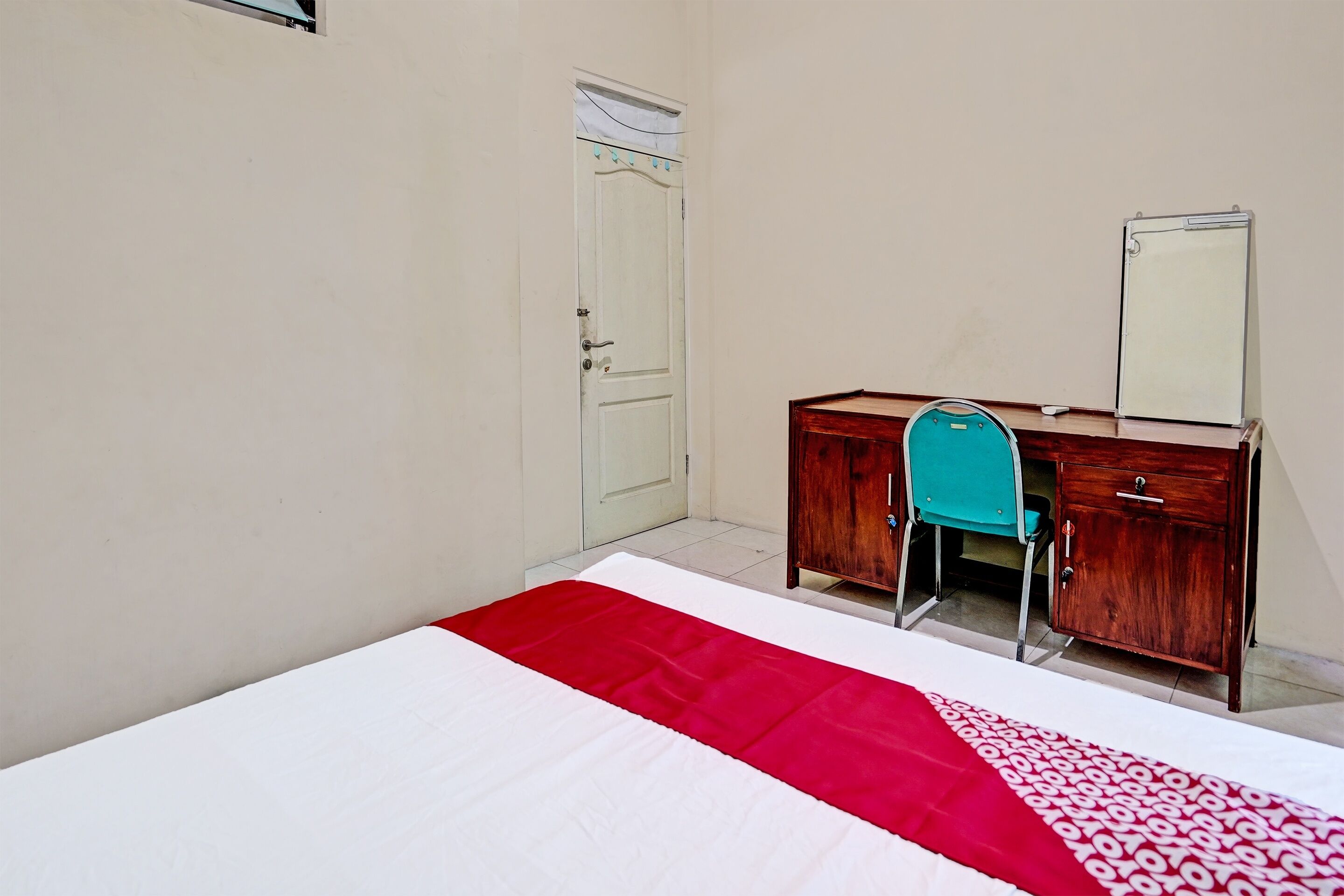 A bedroom with a bed, a wooden dresser, a mirror, and a door.