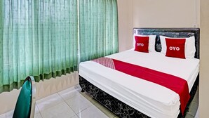A neatly made bed with a white and red bedspread, two red pillows with "OYO" text, and a green curtain.