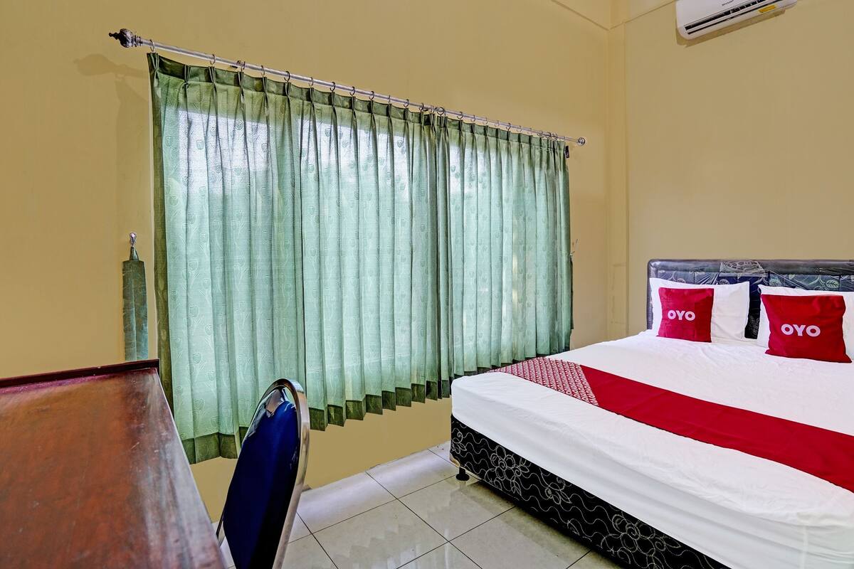 Una camera d'albergo con un letto, una sedia, una tenda e un condizionatore d'aria.