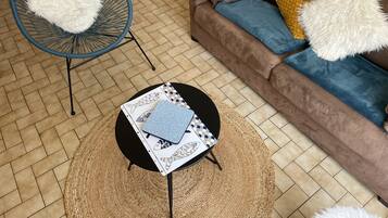 Een woonkamer met een bruine bank, twee witte, zachte fauteuils, een zwarte salontafel met placemats met een vispatroon, en een geweven vloerkleed.