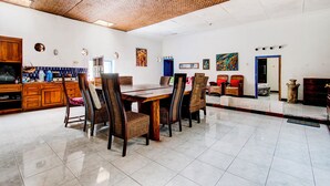 A spacious dining area with a large wooden table and wicker chairs, a kitchen with wooden cabinets, and a patterned ceiling. - Hotel O Prawirotaman Near Keraton Yogyakarta Formerly Chez Laelik Guesthouse (Yogyakarta)