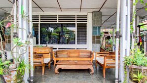 A wooden bench and chairs in a covered outdoor area with potted plants and a window. - Hotel O Prawirotaman Near Keraton Yogyakarta Formerly Chez Laelik Guesthouse (Yogyakarta)