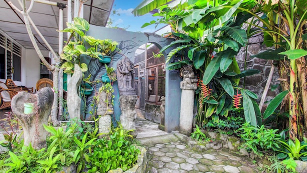 A stone pathway leading through a lush garden with tropical plants and stone statues. - Hotel O Prawirotaman Near Keraton Yogyakarta Formerly Chez Laelik Guesthouse (Yogyakarta)