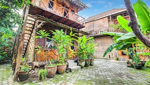 A courtyard with cobblestone flooring, wooden buildings, and potted plants. - Hotel O Prawirotaman Near Keraton Yogyakarta Formerly Chez Laelik Guesthouse (Yogyakarta)