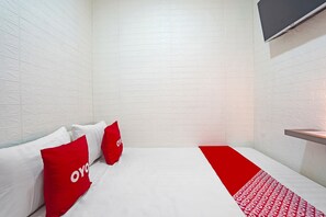 Ein Hotelzimmer mit weißer Ziegelwand, einem Bett mit weißer und roter Bettwäsche sowie einem an der Wand montierten Flachbildfernseher.