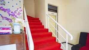 Un escalier dont les marches sont recouvertes d’une moquette rouge, avec une rampe blanche et une porte portant l’inscription « TOILETTES ».