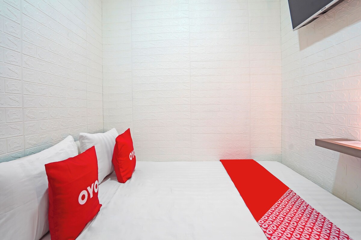 Una camera d'albergo con una parete in mattoni bianchi, un letto con biancheria rossa e bianca e un televisore a schermo piatto fissato al muro.