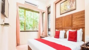 A hotel room with a large bed, a wooden headboard, a painting above the bed, and a window with curtains. - Hotel Subhash (Mumbai)