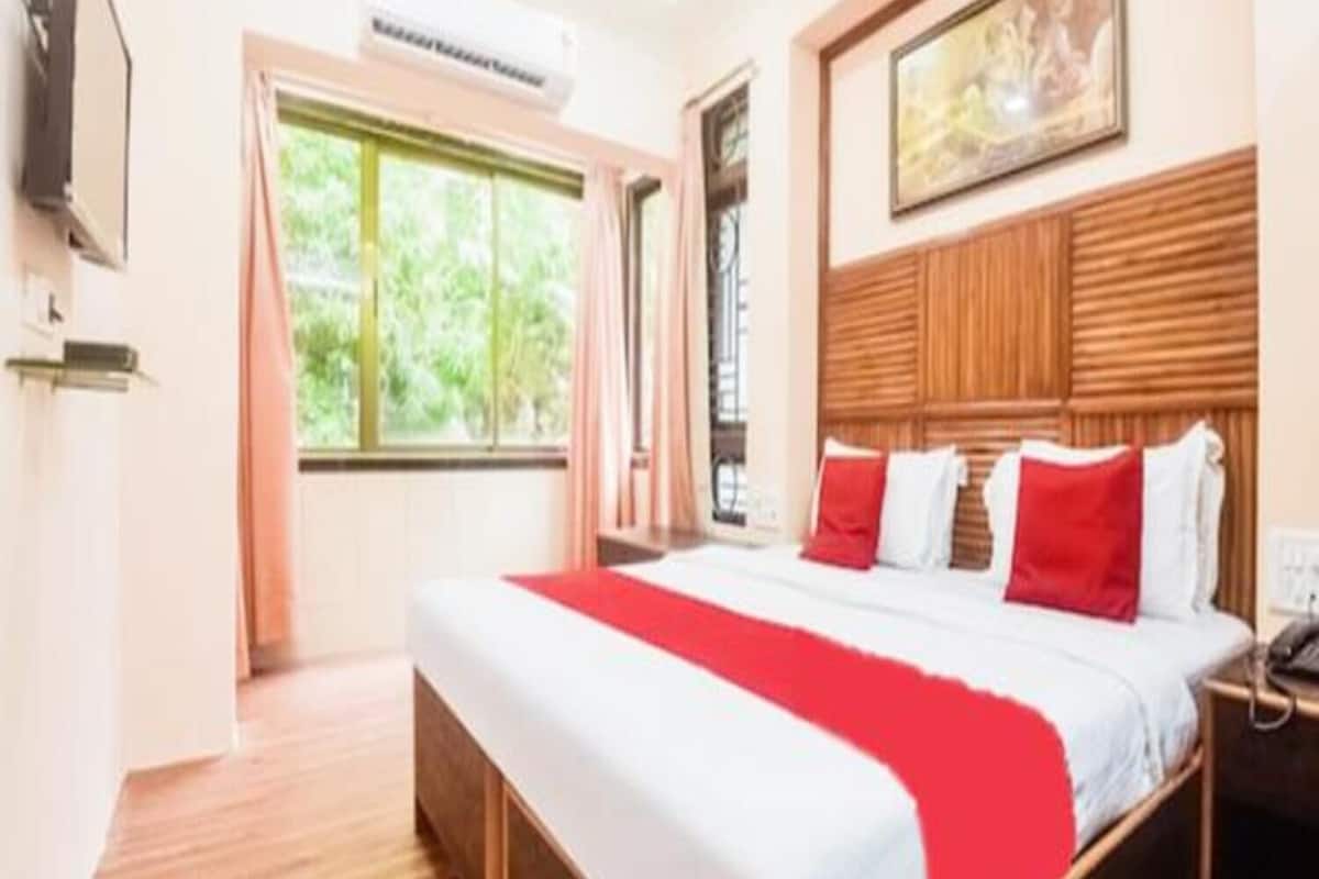 A hotel room with a large bed, a wooden headboard, a painting above the bed, and a window with curtains.