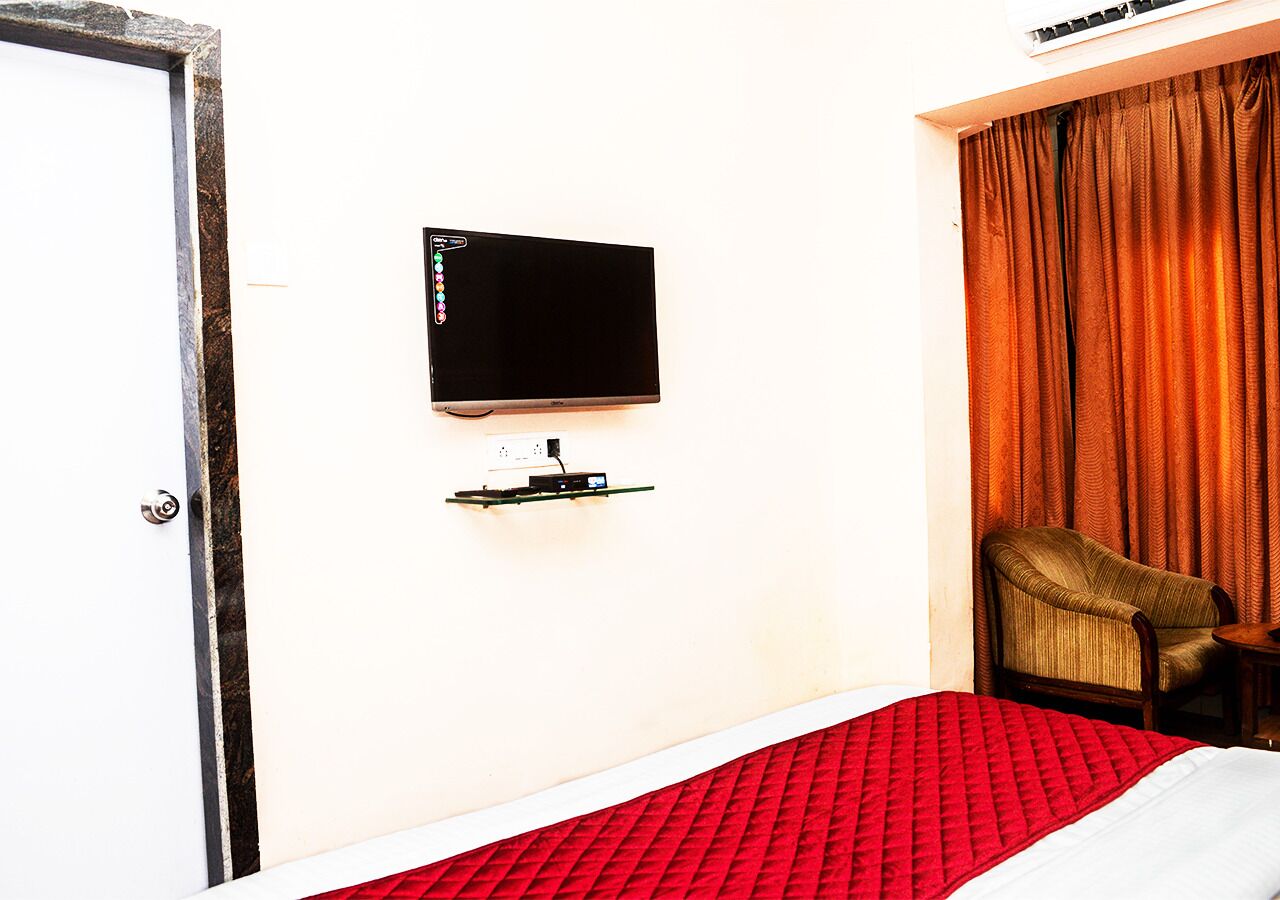 A hotel room with a bed, a television mounted on the wall, a chair, and a window with curtains.